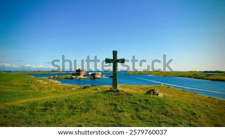 A cross with a rustic brown finish, surrounded by vibrant green grass, is standing in the center of a shimmering body of water