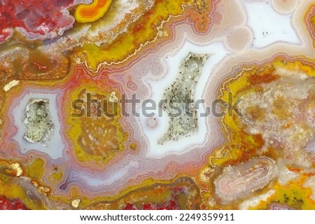 A cross section of the agate stone with quartz geode. Multicolored silica bands colored with metal oxides are visible. Macro photography of the surface of the cut. Origin: Atlas mountains, Morocco.