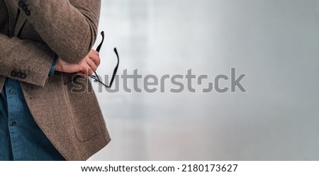Cross section cut off cutoff middle section of human man body with visible hand hands holding glasses eyeglasses crossed hands thinking reduced pose with copy space to right gray background backdrop