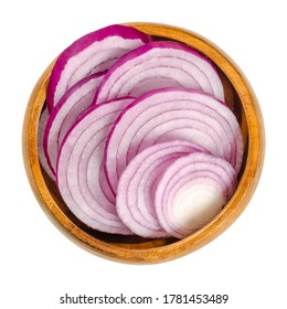 Cross sections of red onions in wooden bowl. Slices of the onion cultivar Allium cepa with purplish red skin and white flesh tinged with red. Closeup from above, over white, isolated macro food photo.