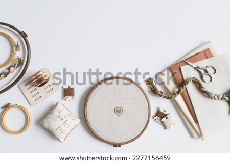 cross stitch embroidery accessories. Linen cloth in hoop on white background with floss, scissors and cloth. Indoor hobby concept.