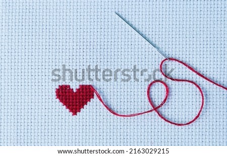 Cross stitch in the shape of a heart with red thread.