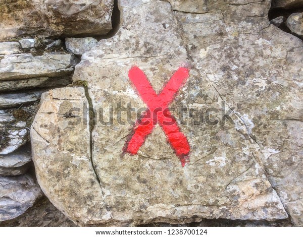 Cross symbol x sign painted in red, cross-shaped\
hiking trail marker on a\
rock