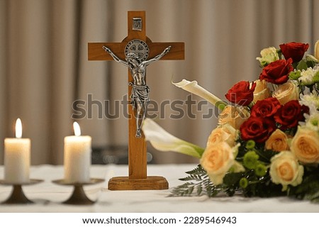 a cross with two candles and a bunch of red and yellow flowers