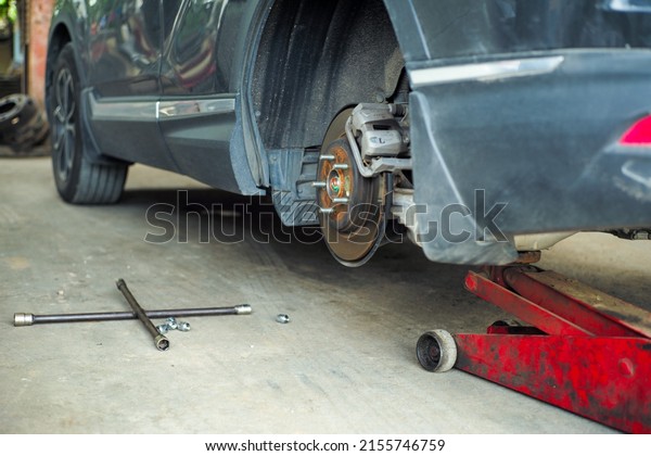 Cross wrench and knots in the garage with car\
without wheel lifted by the\
jack