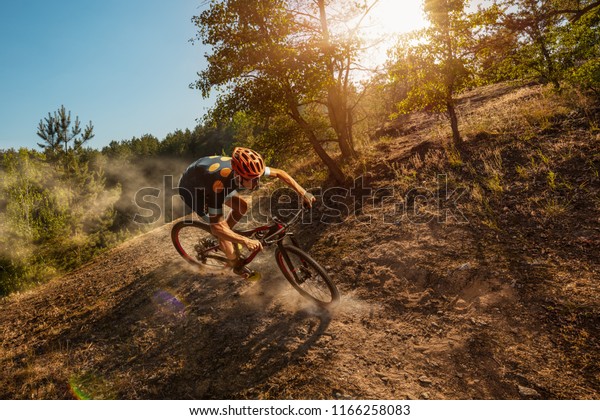 Cross-Country biker on forest trail. Male cyclist\
rides the rock
