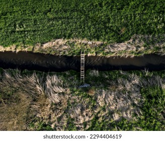 cross-country run through a flooded stream. footbridge with a thinly spaced plank floor. Big water in a narrow channel, video flight over the landscape. seed congestion