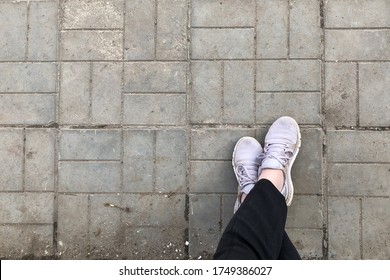 Crossed Feet In Sneakers On The Dirty Sidewalk