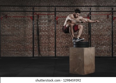 Crossfit Athlete Doing Box Jump Exercise At The Gym. Man Practicing Functional Training. Copy Space