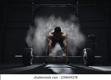 Спортсмен Crossfit готовится поднять тяжелую штангу в облаке пыли в спортзале. Защита от магнизии штанги.