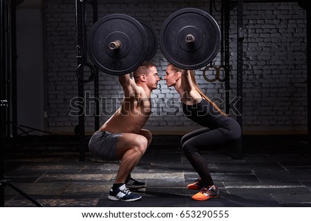 Crossfit lifting bar by woman and man in group workout against brick wall.
