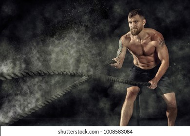 Crossfit training. Man working out with battle ropes at gym