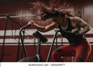 Crossfit woman doing intense cardio training on exercise bike. Her hair is flying from the air flow. Copy space - Powered by Shutterstock