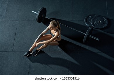 Crossfit woman sitting on floor at gym looking into the distance, resting after cross-fit workout with barbell View from above Concept of power, strength, healthy lifestyle, sport Copy free space - Powered by Shutterstock