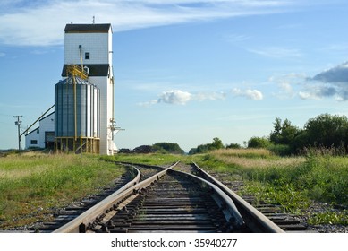 A crossroad section of the railroad tracks with one side going to a grain elevator and the other going straight and disappearing in the distance