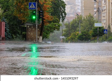 At The Crossroads Of The Road, The Green Light Of A Traffic Light Is Lit In The Pouring Rain On A City Street.