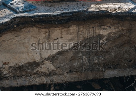 Cross-section of a soil collapse under a broken asphalt road. Detailed view of ground layers and pavement damage at a city repair site. Geotechnical background of a street sinkhole.