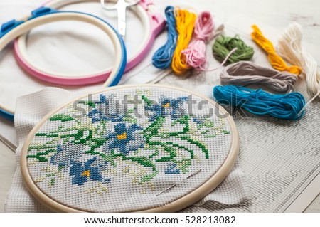 Cross-stitch set : hoop with embroidered flowers pattern, scissors, canvas and colorful yarn. Selective focus. Freelance, hobby, handmade home decor concept