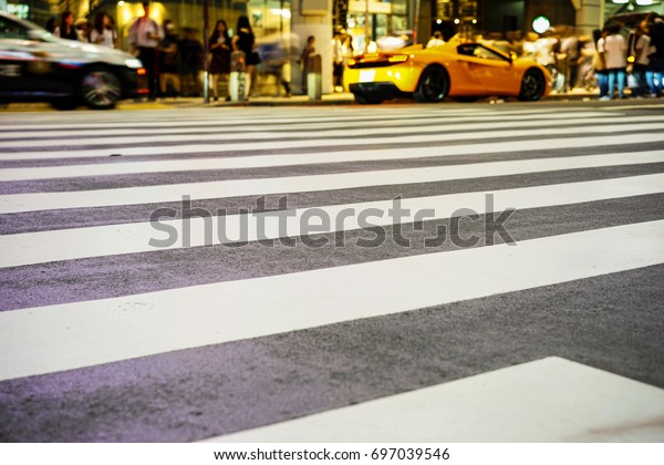 Crosswalk and\
pedestrian at modern city zebra crossing street with fast moving\
car lights in the Shibuya\
Crossing