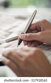 Crossword Puzzle Close-up. Hand Of A Young Woman Doing A Crossword In A Newspaper