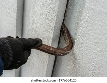 Crowbar Held In Hands While Breaking Down The Wooden Wall Of A Building Being Demolished.