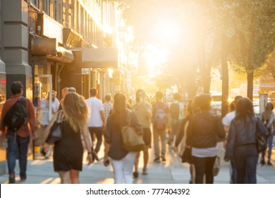 Crowd Of Anonymous Men And Women Walking Down An Urban Sidewalk With Bright Glowing Sunlight In The Background On A Busy Street In Downtown Manhattan, New York City 