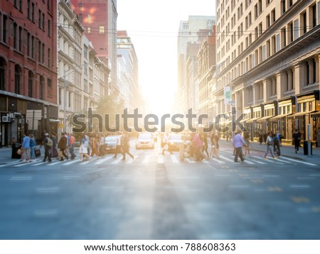 Crowd of anonymous people crossing the street at a busy intersection in Manhattan, New York City with the bright glow of sunset in the background