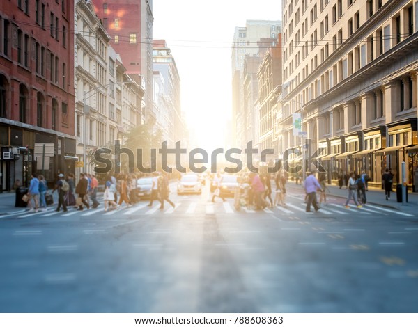 Crowd of anonymous people crossing the street\
at a busy intersection in Manhattan, New York City with the bright\
glow of sunset in the\
background