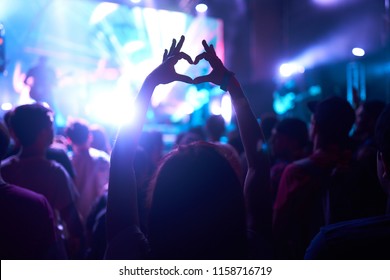 Crowd Of Audience At During A Concert With Silhouette Of A Heart Shaped Hands Shadow
                    