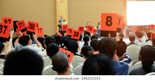 Crowd of bidders holding their numbered bidding paddles at an auction