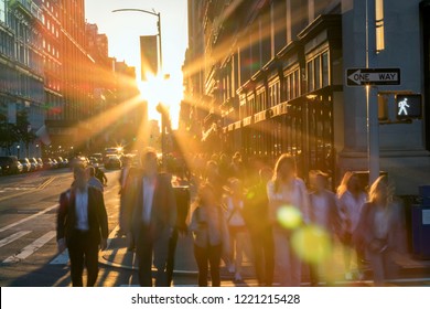 Crowd Of Blurred People Crossing A Busy Intersection On 5th Avenue In New York City With The Bright Light Of Sunset In The Background