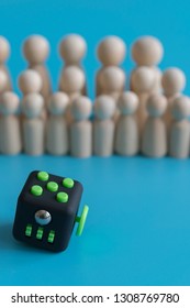 Crowd Calm Concept. Answer How To Calm The Crowd. Fidget Cube Stress Reliever And Wooden Figures On A Blue Background. Vertical Photo.