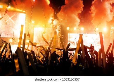 Crowd Of Concert Stage Lights And People Fan Audience Silhouette Raising Hands Or Glow Stick Holding In The Music Festival Rear View With Spotlight Glowing Effect And Smoke