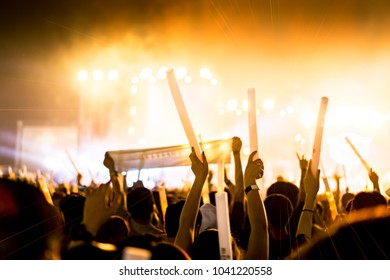 Crowd Of Concert Stage Lights And People Fan Audience Silhouette Raising Hands Or Glow Stick Holding In The Music Festival Rear View With Spotlight Glowing Effect And Smoke