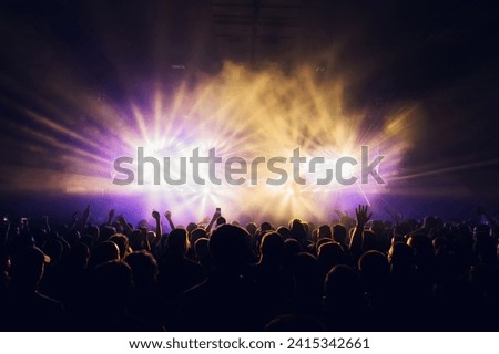 Crowd dancing and having fun at night on a music festival. There are stage purple and yellow lights. Silhouettes of people having fun, dancing on music festival. Nightlife.