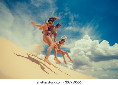 Crowd of friends jumping on sandy beach with their arms raised against blue sky - Powered by Shutterstock