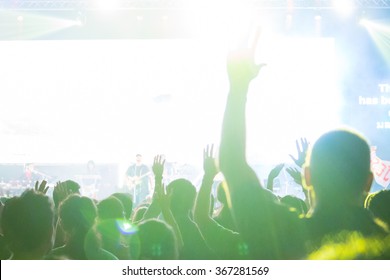 A crowd level view of hands raised from the spectating crowd interspersed by colorful spotlights and a smokey atmosphere - Shutterstock ID 367281569