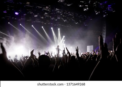 Crowd on music show, happy people with raised hands. White stage light. Frontman on stage