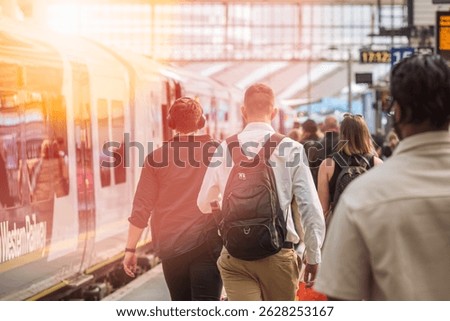 A crowd of passengers walking to board a train at London Waterloo station, with warm sunlight shining on the platform