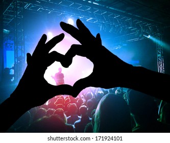 A Crowd Of People At A Concert With A Heart Shaped Hand Shadow