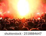 Crowd of people enjoys and cheering music concert in front of bright stage lights. Happy audience dance and raise hands.