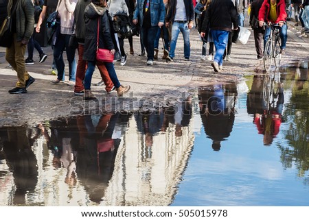 crowd of people on the move in the city, reflecting in a puddle