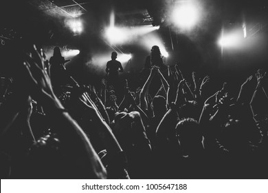 Crowd of people on a rock concert with the hands raised up looking to the rock band on a stage, black and white shot