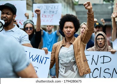 Crowd of people participating in anti-racism protest. Focus is on black woman with raised fist.