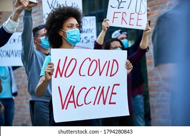 Crowd Of People Protesting Against Coronavirus Vaccination. Focus Is On Black Woman Carrying Banner With 'no COVID Vaccine' Inscription. 