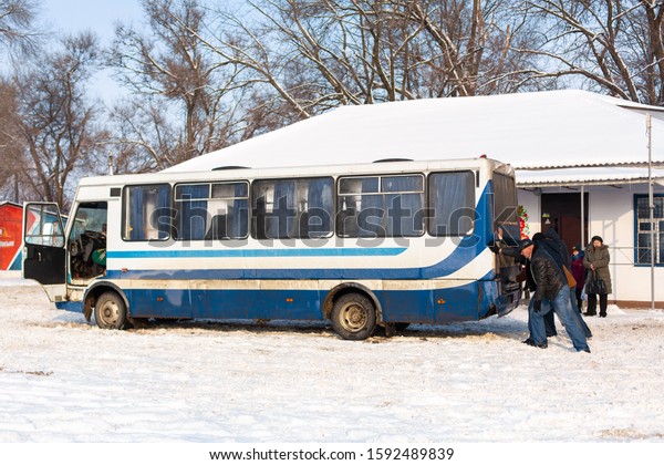 A crowd of people are pushing a bus that is\
stuck in the snow. Severe weather conditions. Snow paralyzes\
traffic. Kobelyaky / Ukraine -\
01.09.2019