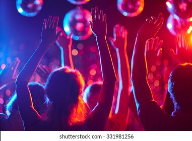Crowd of people with raised arms dancing in night club