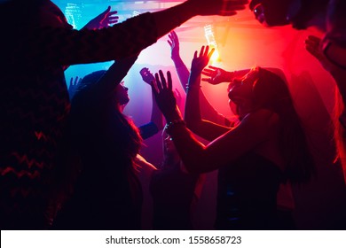 A crowd of people in silhouette raises their hands on dancefloor on neon light background. Night life, club, music, dance, motion, youth. Purple-pink colors and moving girls and boys.