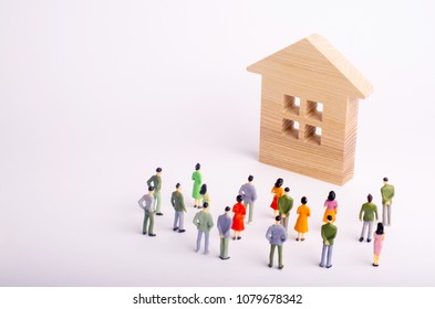 A Crowd Of People Standing And Looking At A Wooden House On A White Background. Buying And Selling Of Real Estate, Rent. Affordable Housing. A Group Of Tourists Visiting The Sights. Selective Focus