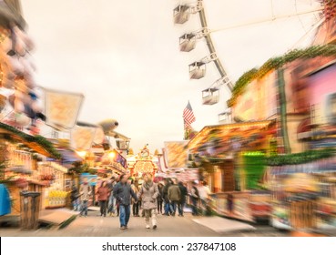 Crowd Of People Walking At Luna Park On A Radial Zoom Defocusing - Multicolored Fun Stands At German Christmas Market - Ferris Wheel And Colorful Wooden Houses At Berlin Amusement Area In Winter Time